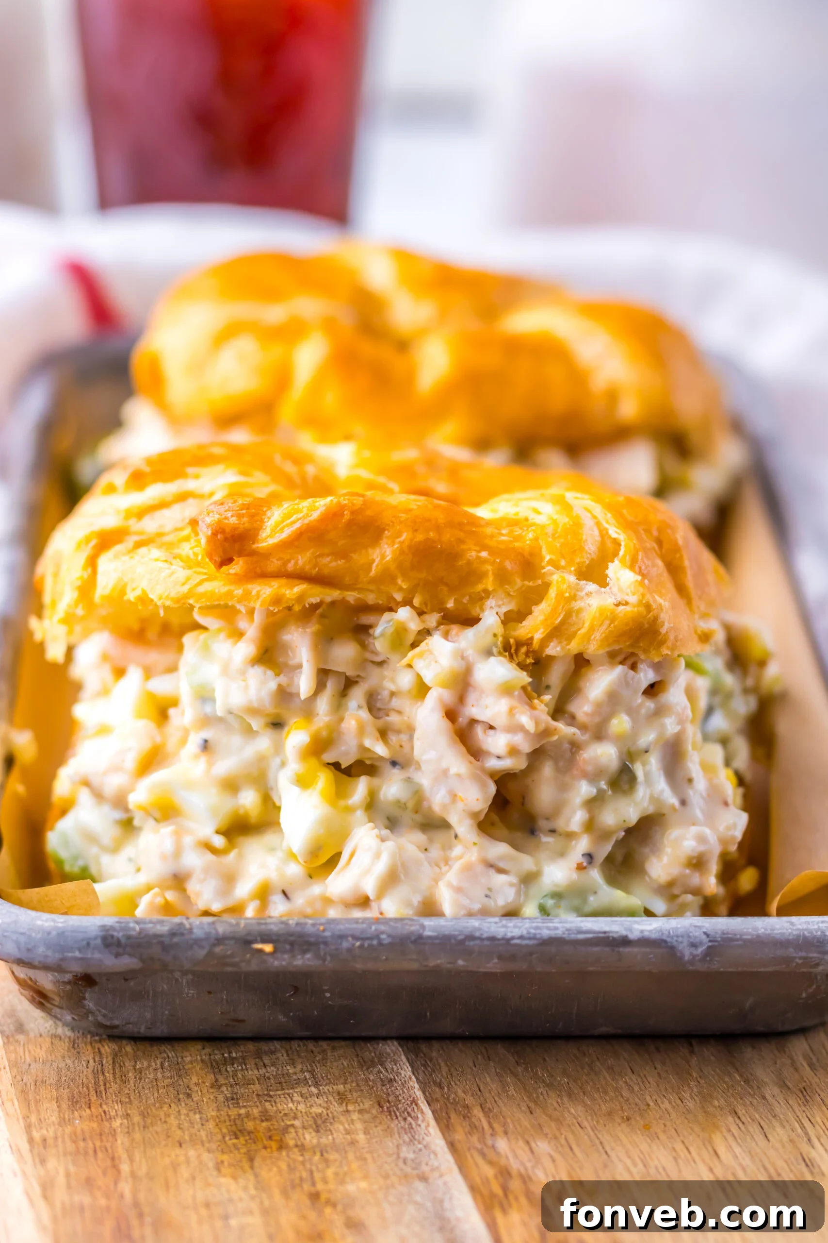 Close up shot of chicken salad on a white croissant on a tin tray.  