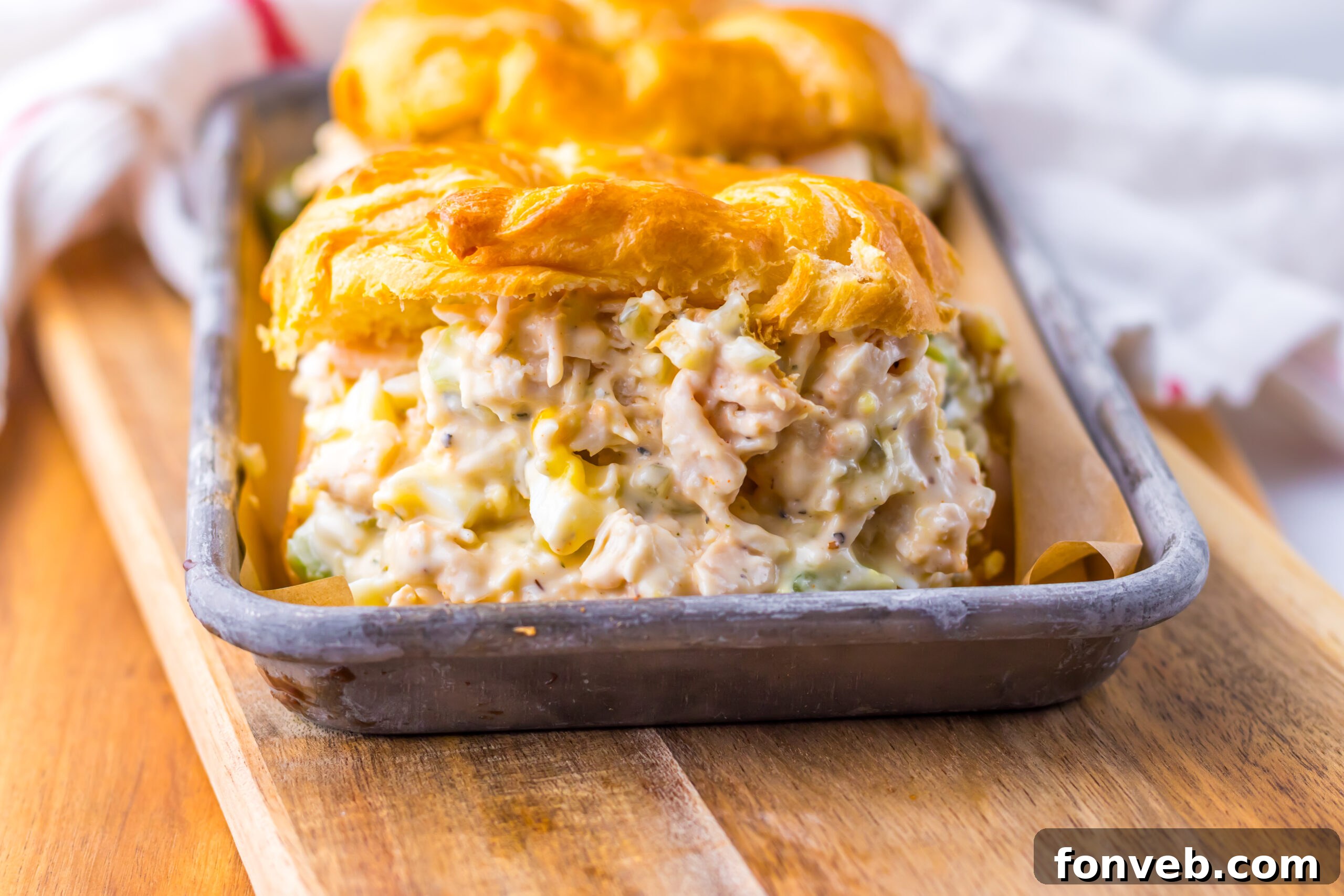 front view of a large chicken salad sandwich on a white croissant on a tin tray.  