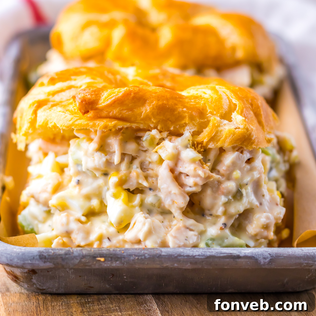 Close up shot of chicken salad on a white croissant on a tin tray.  