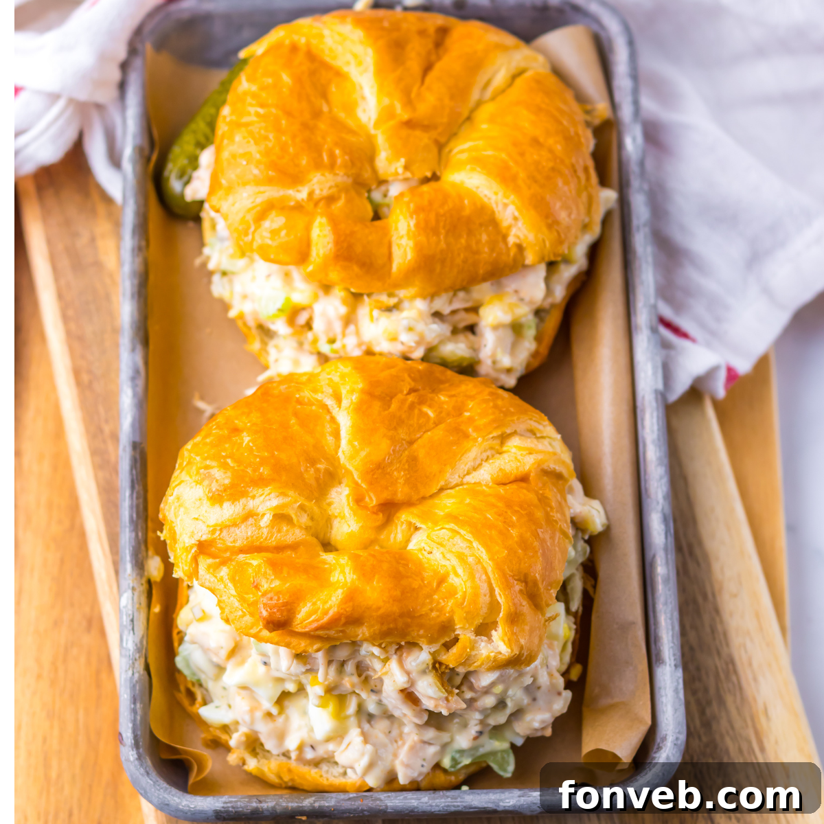 Overhead shot of chicken salad on a white croissant on a tin tray.  