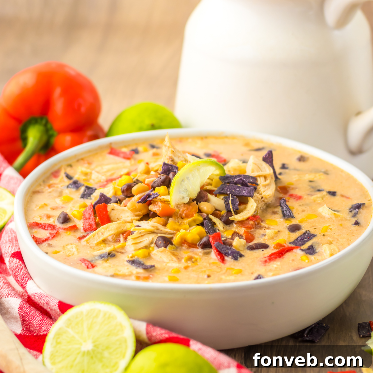 A side view of a steaming bowl of Slow Cooker Tortilla Soup, garnished with a sprinkle of fresh cilantro and crispy tortilla strips, resting on a white and red checkered napkin.