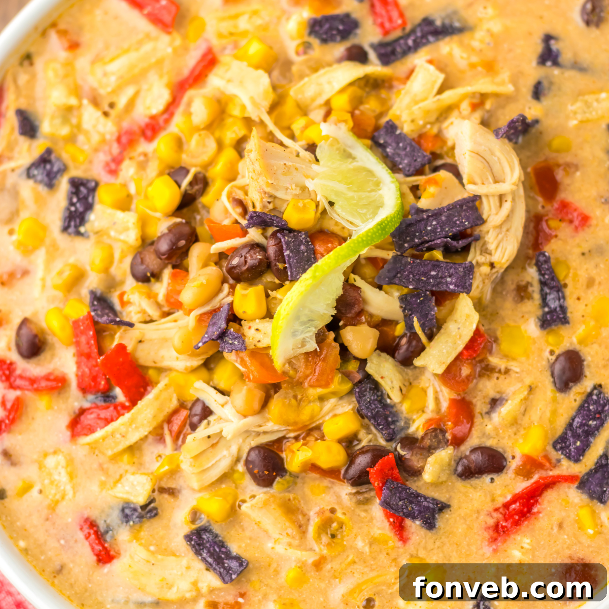 A close-up overhead view of Slow Cooker Tortilla Soup, richly adorned with toppings including vibrant corn kernels, savory black beans, and crispy tortilla chips.