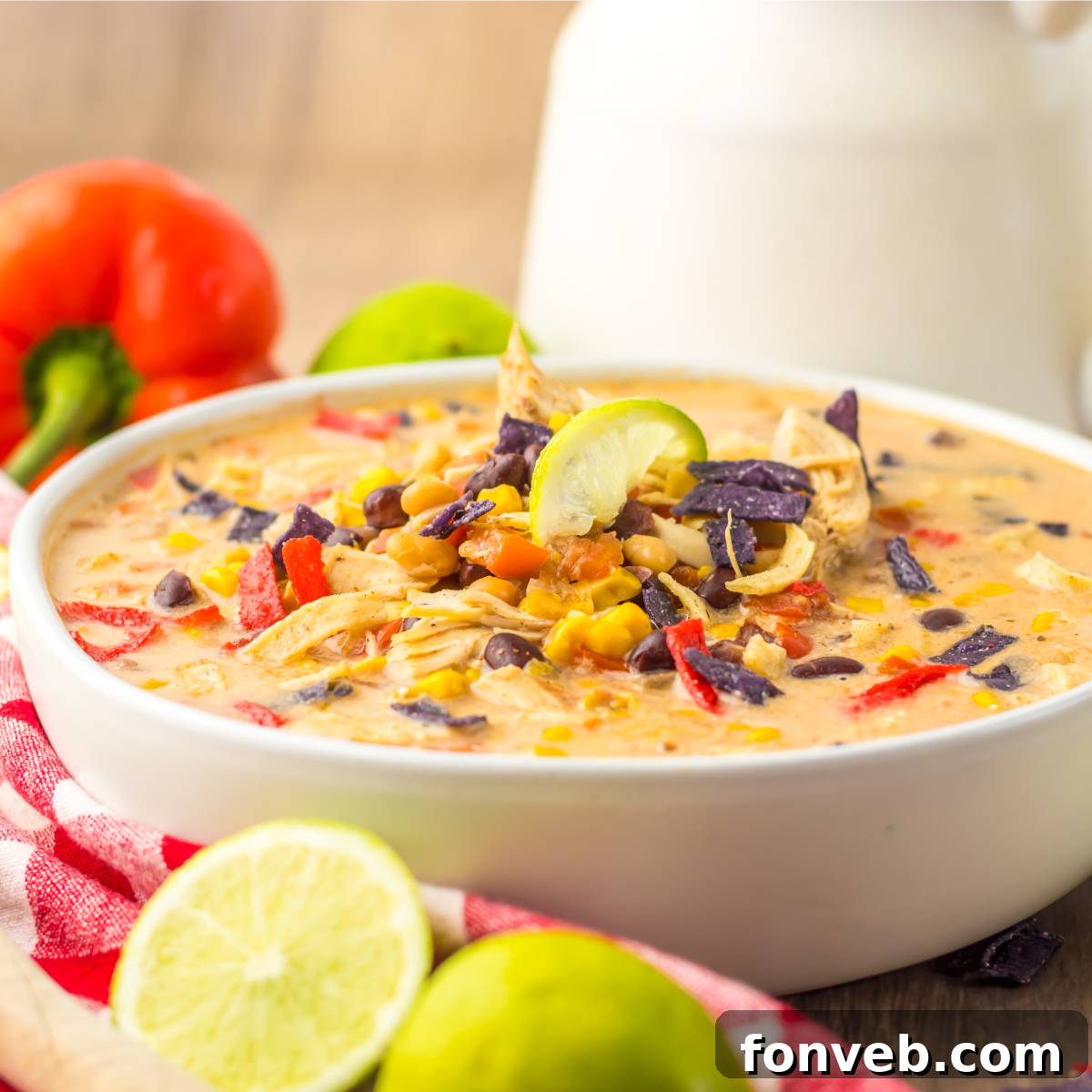 A close-up side view of a white bowl filled with Slow Cooker Tortilla Soup, generously topped with crispy tortilla chips, vibrant corn kernels, and hearty black beans.