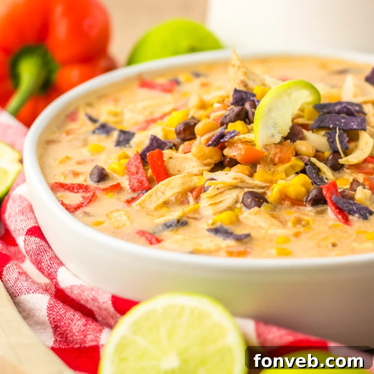 A close-up side view of a vibrant Slow Cooker Tortilla Soup in a white bowl, richly garnished with a mound of crunchy tortilla chips.
