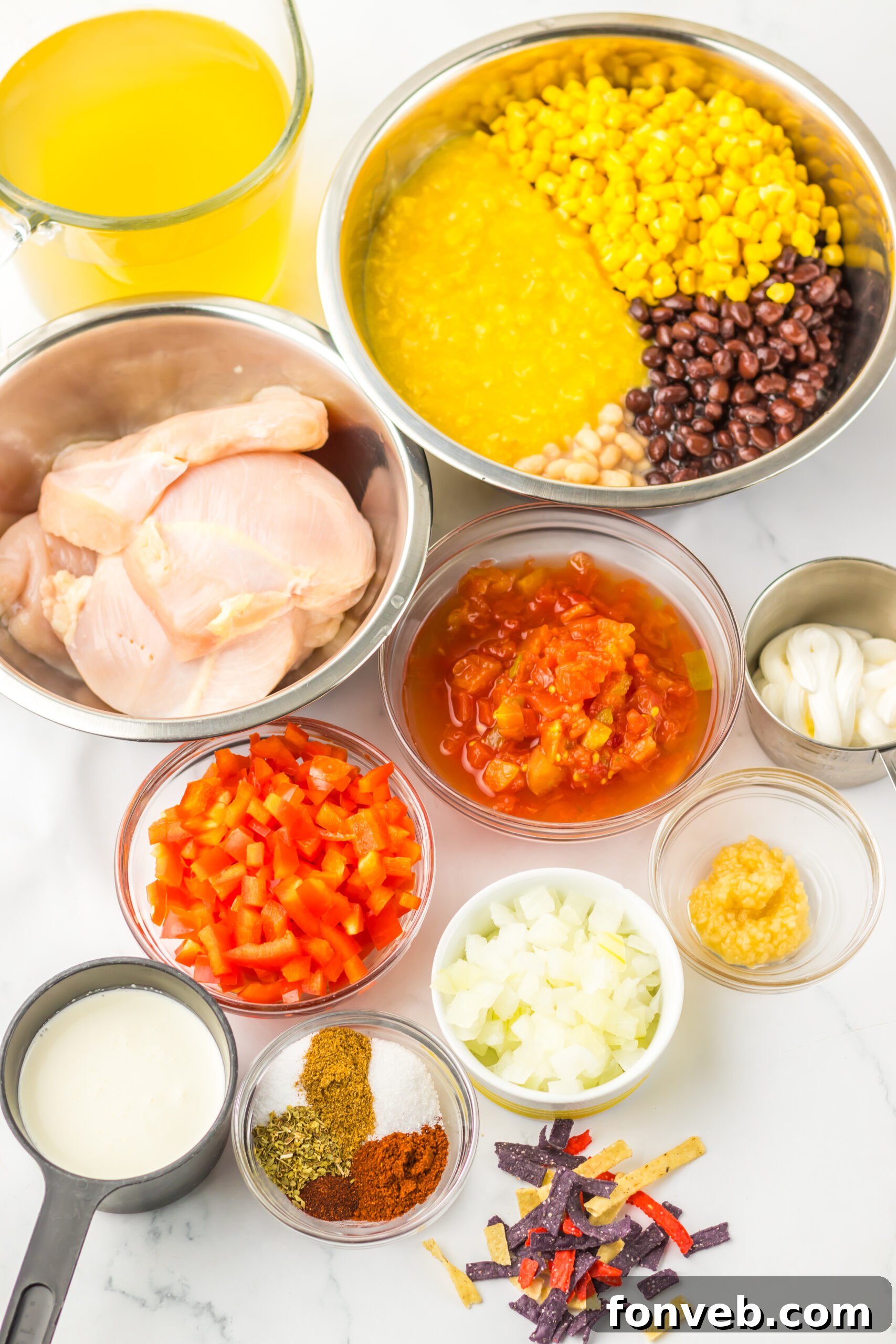 A beautiful flat lay of fresh ingredients for tortilla soup, including chicken breasts, corn, beans, onions, and various spices, all arranged on a elegant marble countertop. 

