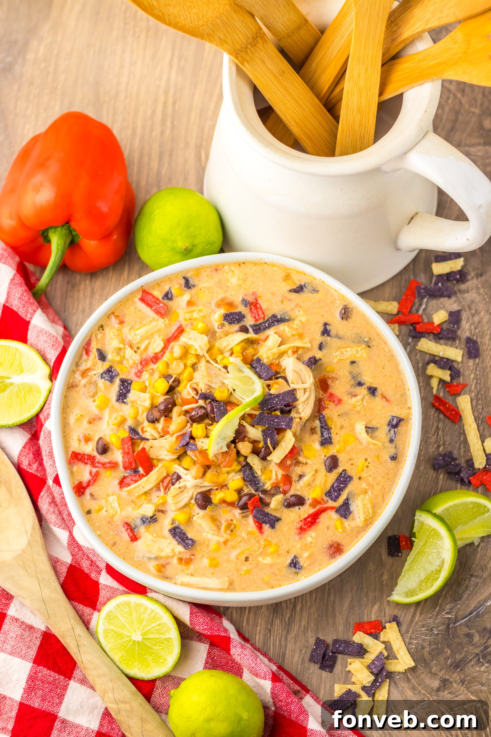 A close-up side view of a white bowl filled with Slow Cooker Tortilla Soup, adorned with crispy tortilla chips and fresh lime slices for garnish.