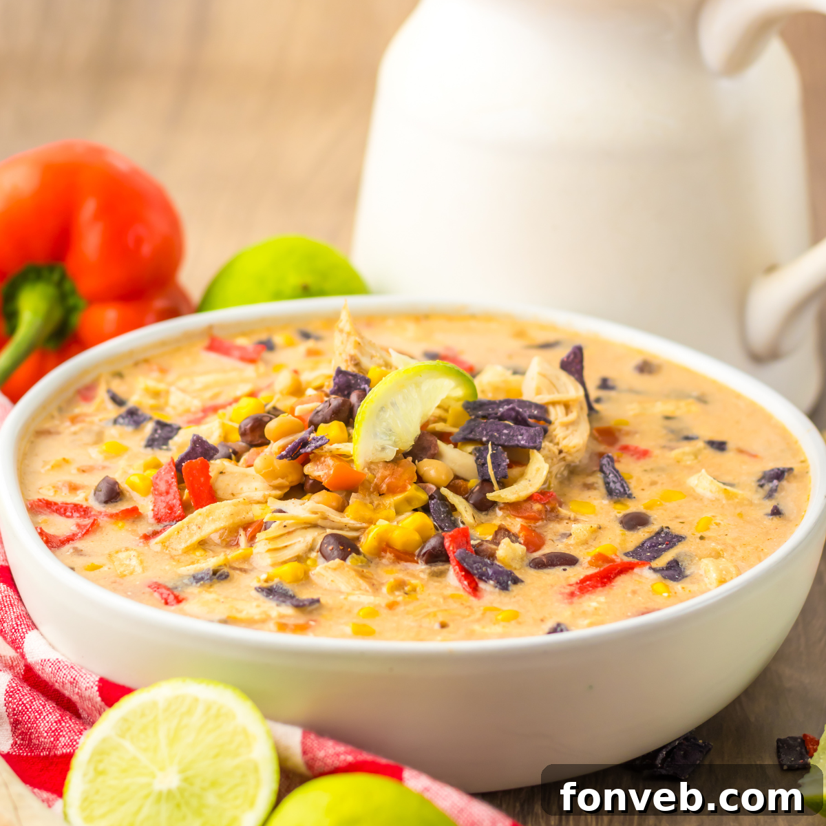 A close-up side view of a white bowl filled with Slow Cooker Tortilla Soup, generously topped with crispy tortilla chips.