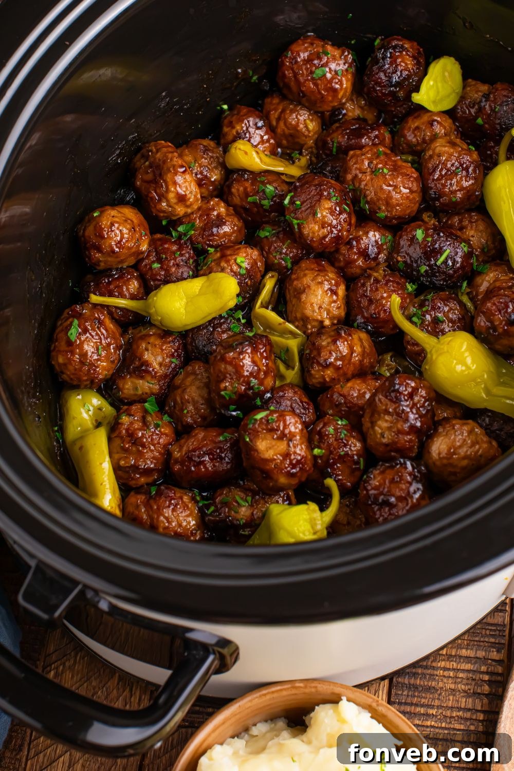 CrockPot angled to side on table with Mississippi meatballs inside and peppers 