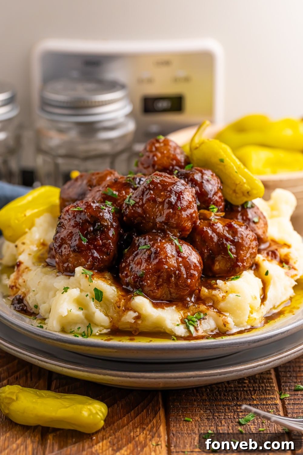 Crockpot Mississippi Meatballs on a stack of plates with more peppers to side and CrockPot behind it on table 