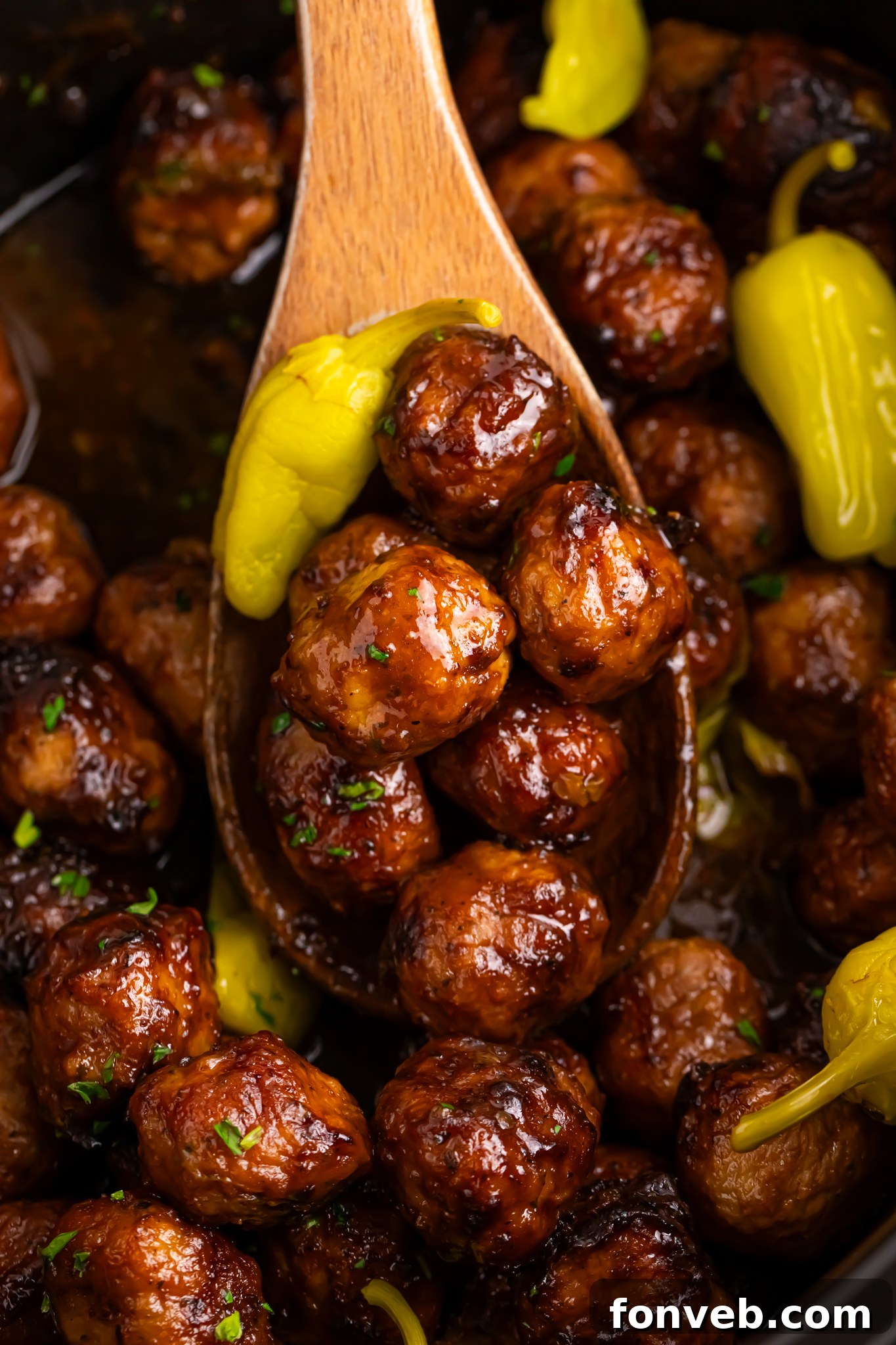 wooden spoon being held above Crockpot with Mississippi meatballs in it 