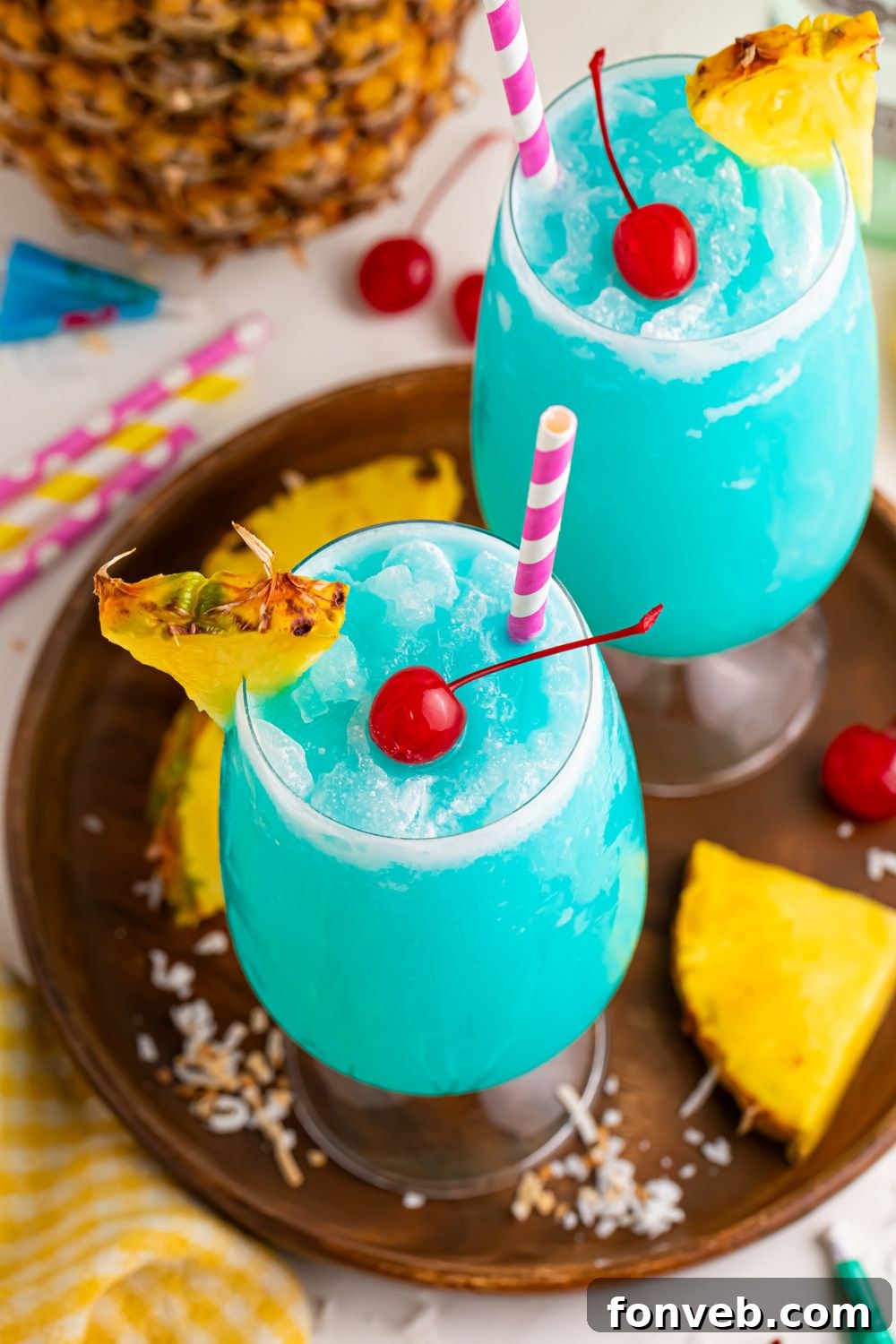 Frozen Blue Hawaiian Cocktails with coconut and pineapple around the glasses and straws 