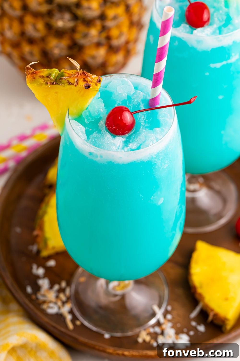 Frozen Blue Hawaiian Cocktails on table with a close up of class to see the cherry in center of drink and pineapple wedge on side of glass 
