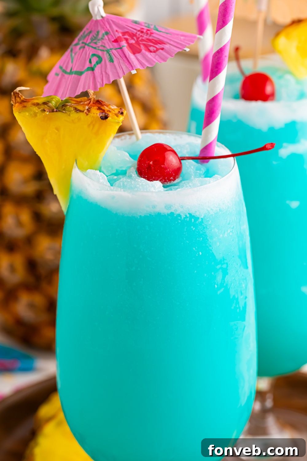 close up of Frozen Blue Hawaiian Cocktails in glasses with coconut rim, pineapple wedge and maraschino cherry 