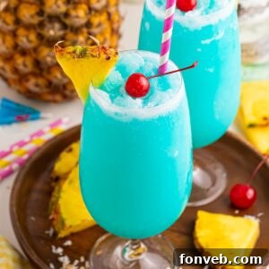 Frozen Blue Hawaiian Cocktails on serving tray with sliced pineapple and cherries around it on table