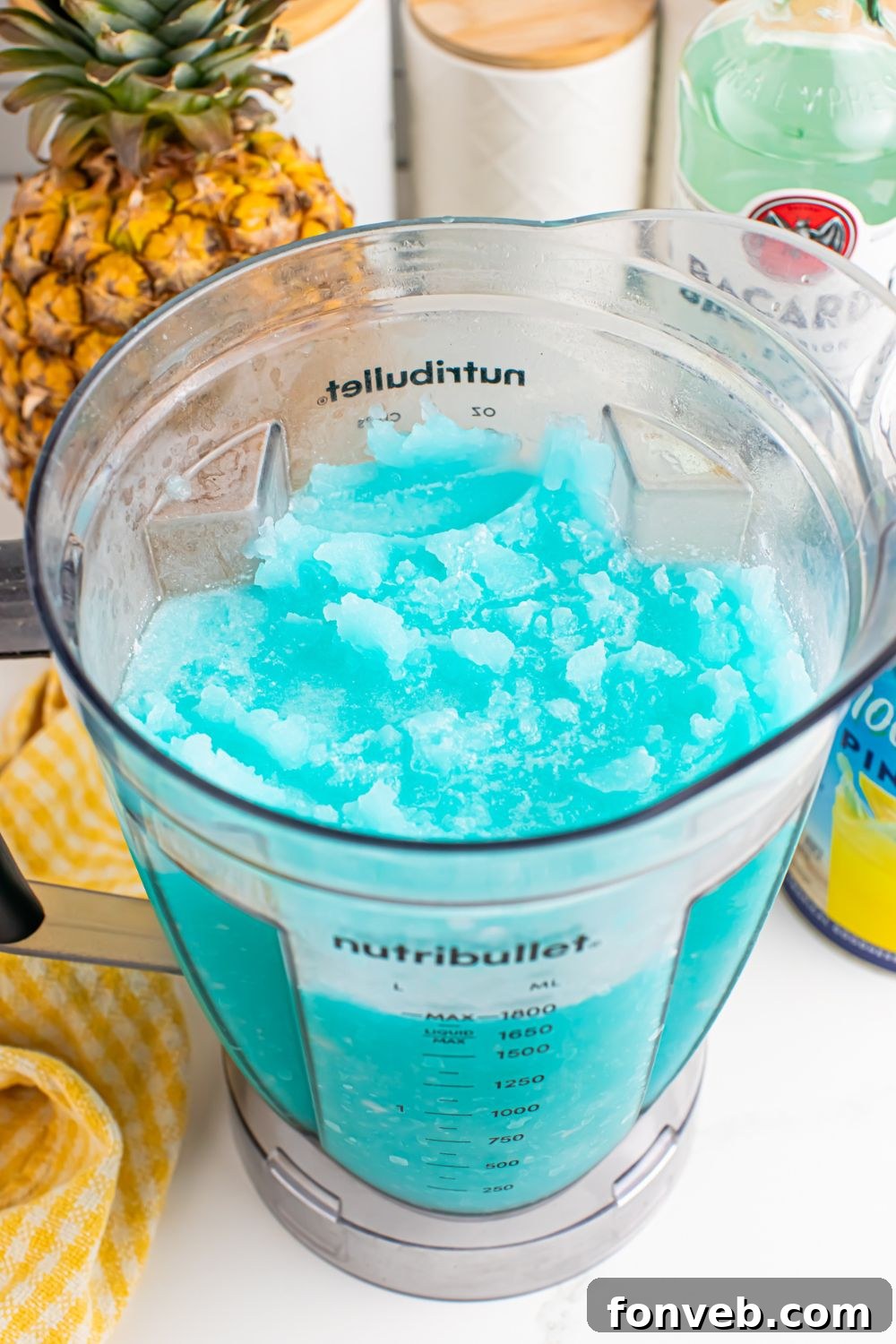 Frozen Blue Hawaiian Cocktail in a blender with ingredients for drink behind it on table 