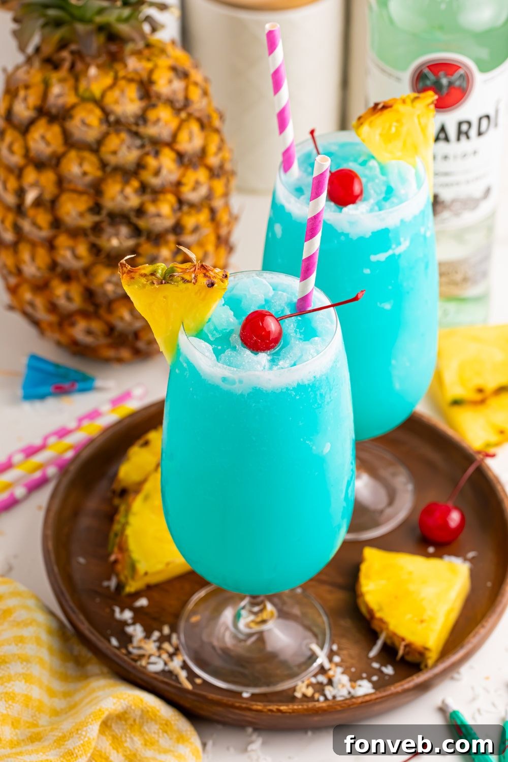 Frozen Blue Hawaiian Cocktails in glasses on table with a whole pineapple in background and sliced pineapple around table 