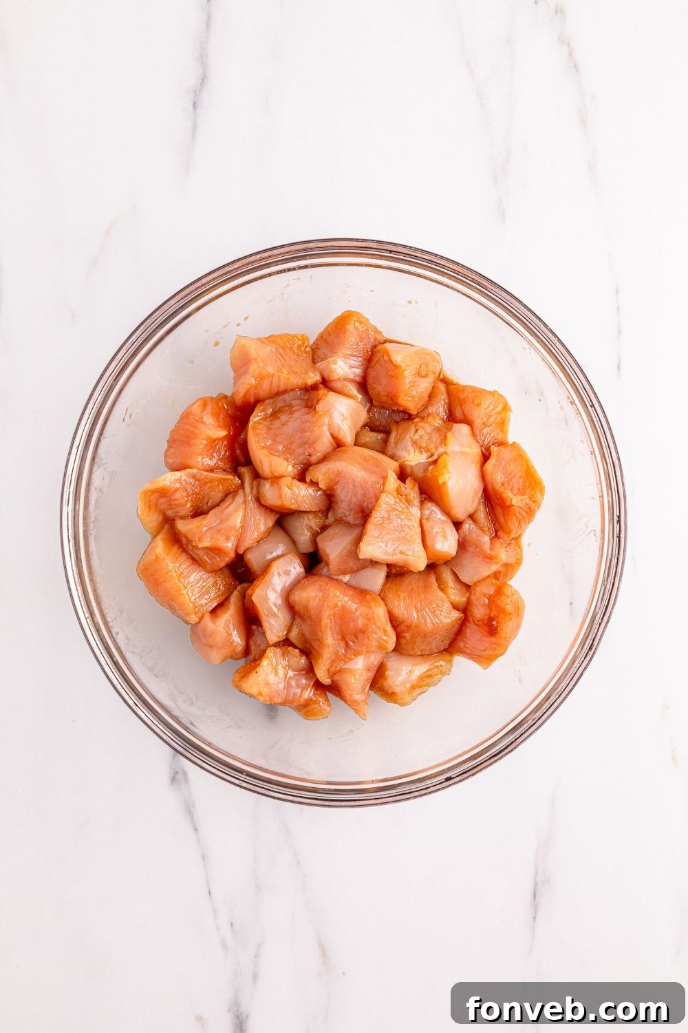 A glass bowl holds diced and seasoned raw chicken, perfectly marinated and prepared for cooking in the Kung Pao Chicken recipe.
