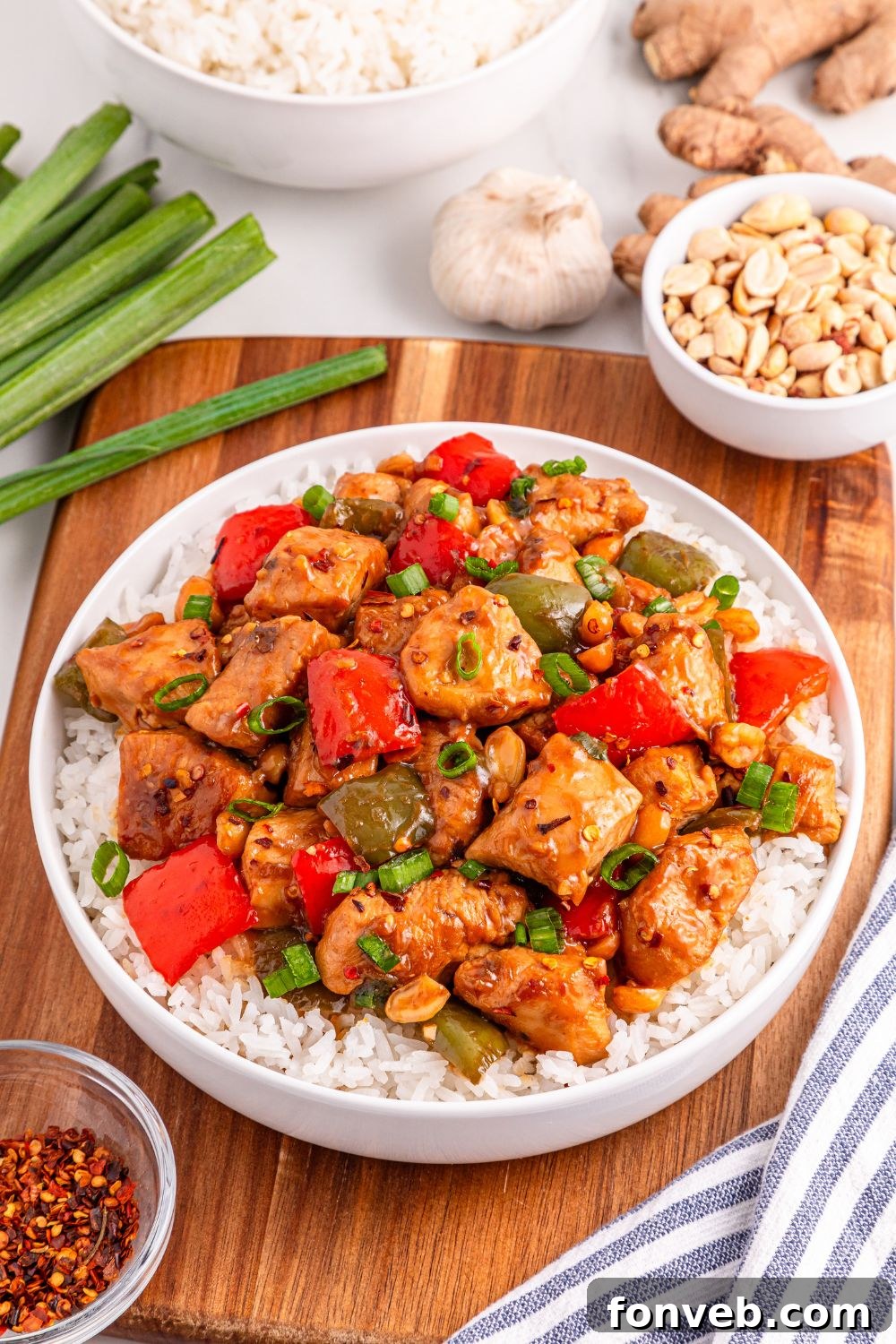 A plate of Better Than Takeout Kung Pao Chicken and rice, garnished with fresh green onions and garlic on the side.