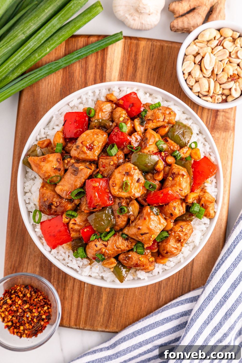 A plate of Better Than Takeout Kung Pao Chicken, beautifully presented with a garnish of nuts, green onions, ginger, garlic, and red pepper flakes scattered around.