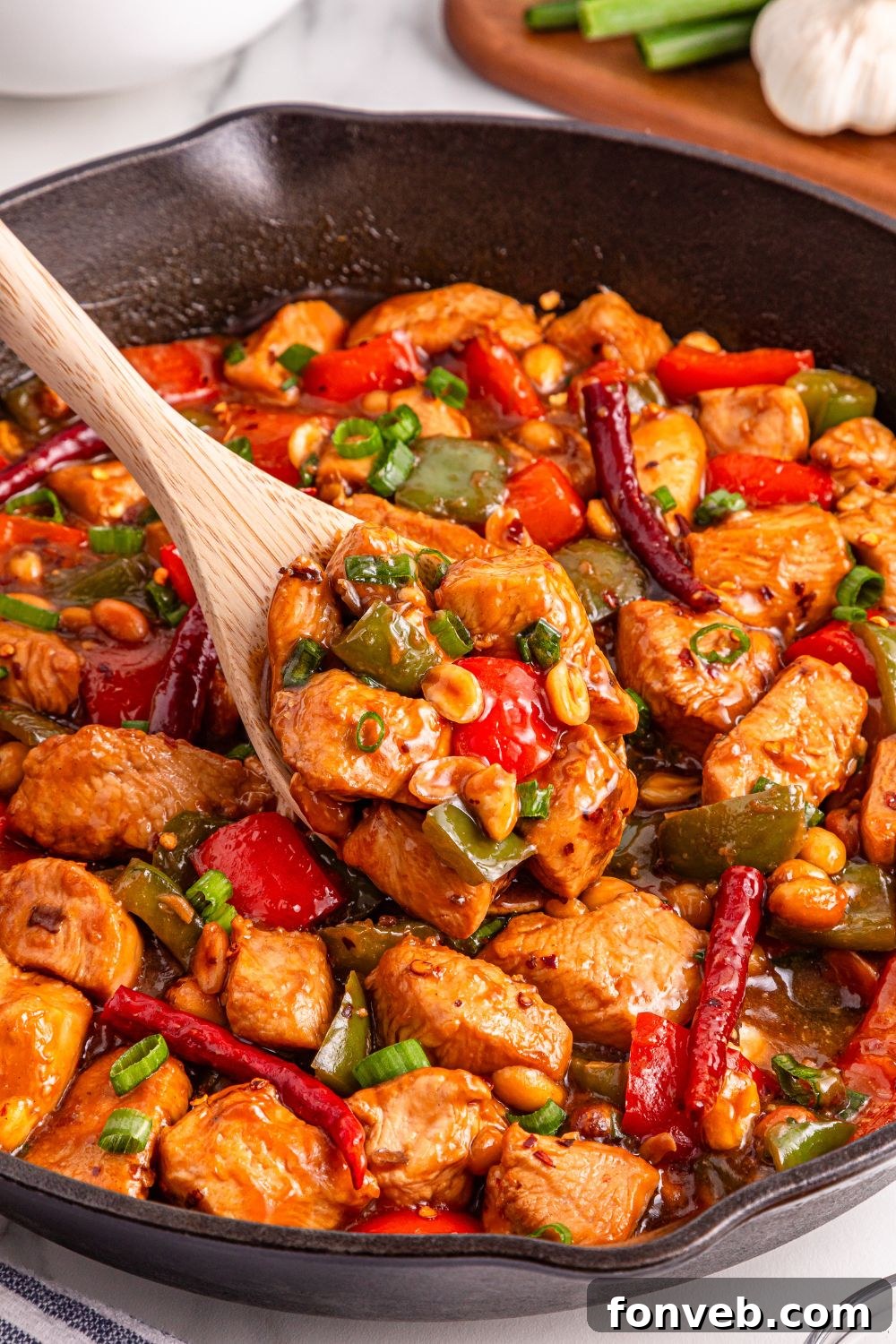 Better Than Takeout Kung Pao Chicken simmering in a skillet, with a spoon scooping up a portion of the savory chicken and vegetables.