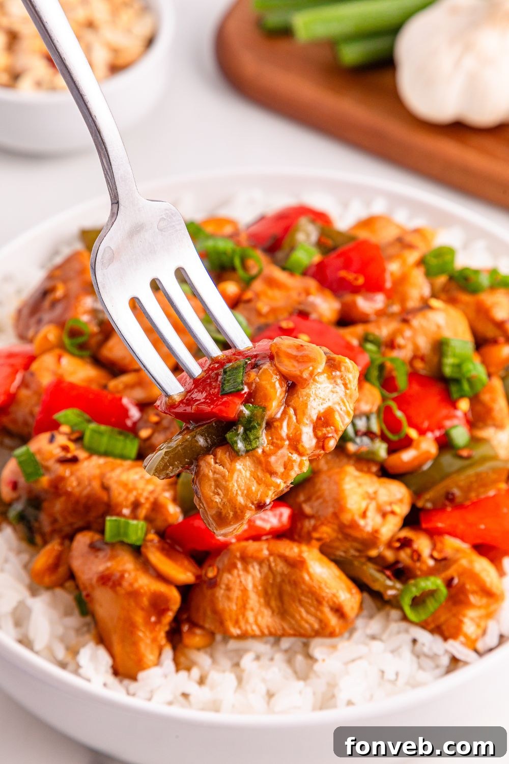 Better Than Takeout Kung Pao Chicken plated with a bed of rice underneath and a fork resting in the chicken, highlighting its deliciousness.