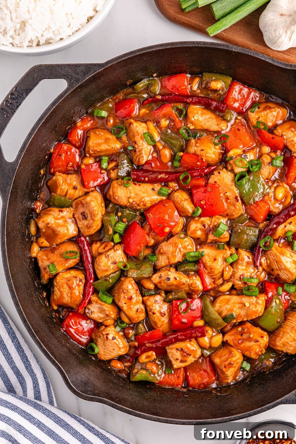A delightful spread featuring Better Than Takeout Kung Pao Chicken in a skillet, accompanied by fresh green onions and garlic, ready for preparation.