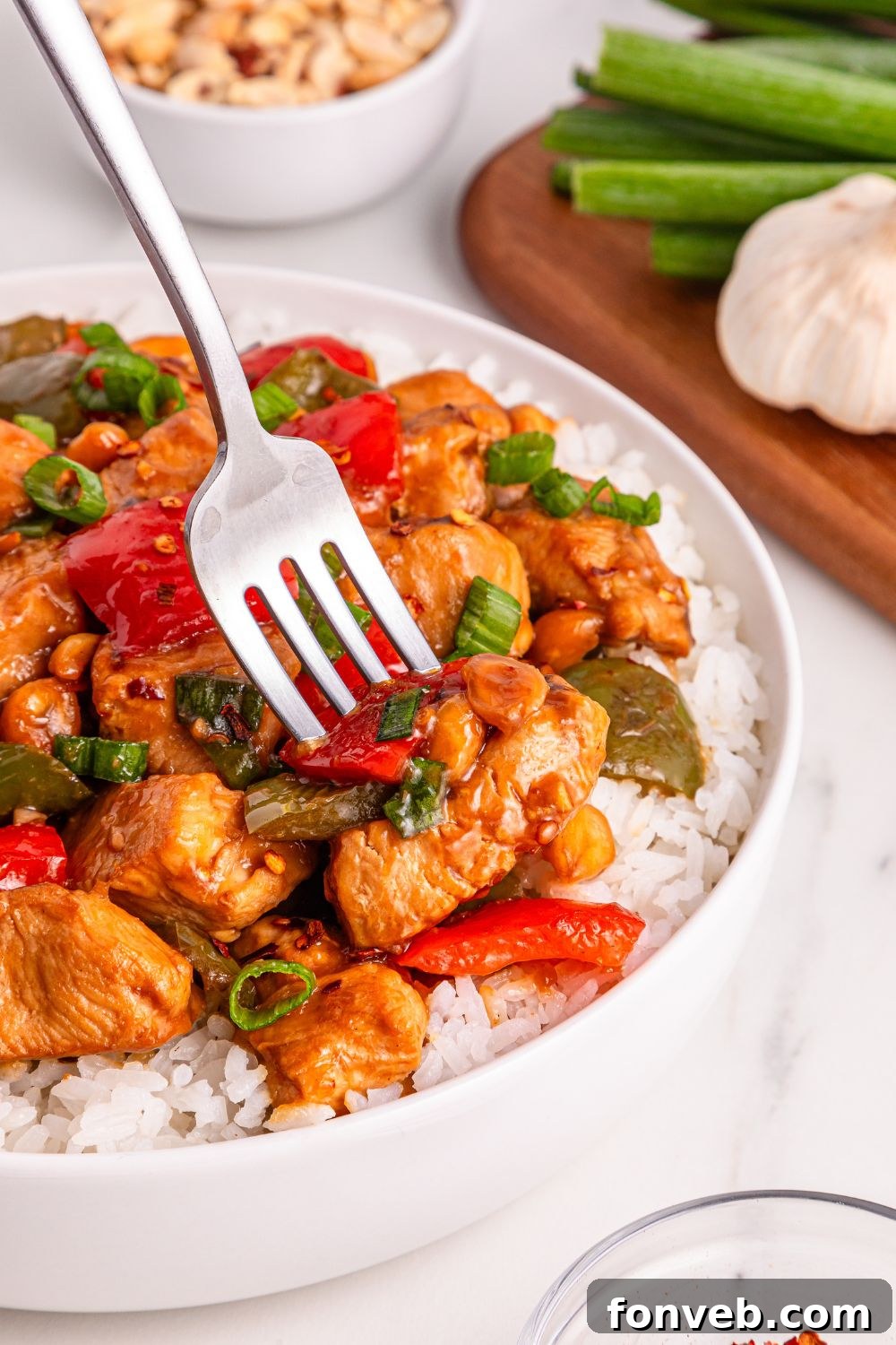 A plate of Better Than Takeout Kung Pao Chicken with rice, featuring a fork ready to pick up a juicy piece of chicken, highlighting the rich sauce.