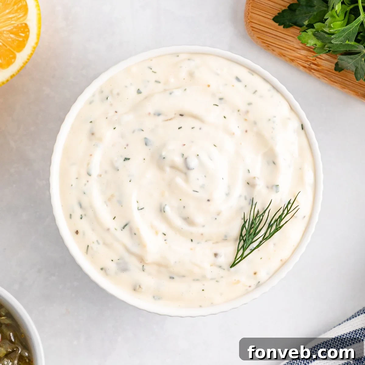 Effortless Homemade Tartar Sauce Beats Store Bought 3 Easy Homemade Tartar Sauce presented in a pristine white bowl, garnished with a sprig of fresh dill, on a rustic wooden table.