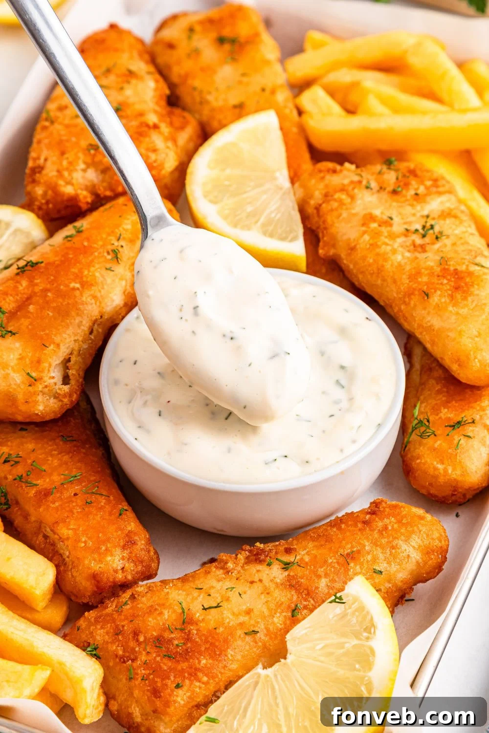 Effortless Homemade Tartar Sauce Beats Store Bought 25 A bowl of tartar sauce with a spoon dipping in, surrounded by crispy fish fillets and golden fries, creating an inviting scene.