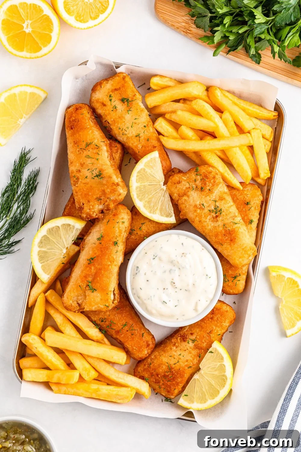 Effortless Homemade Tartar Sauce Beats Store Bought 5 A beautifully arranged platter featuring golden fish and chips, accompanied by a small bowl of homemade tartar sauce and fresh lemon wedges, all on a serving tray.