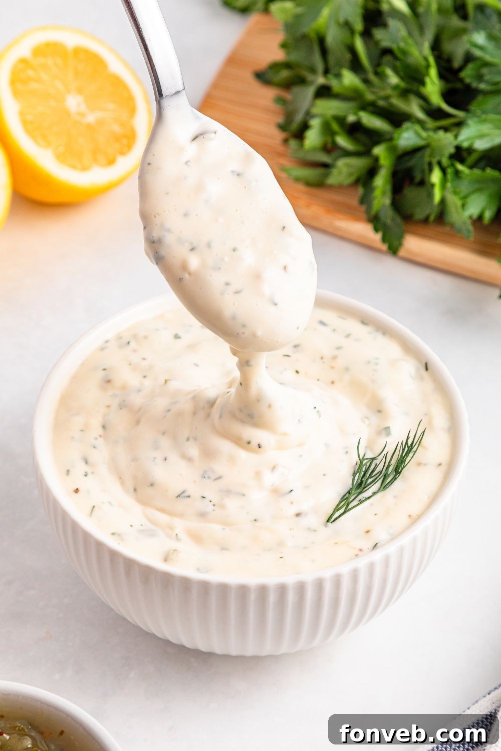 Effortless Homemade Tartar Sauce Beats Store Bought 6 Close-up of Easy Homemade Tartar Sauce in a white bowl, with a spoon gently lifting a portion, highlighting its creamy consistency and embedded herbs.