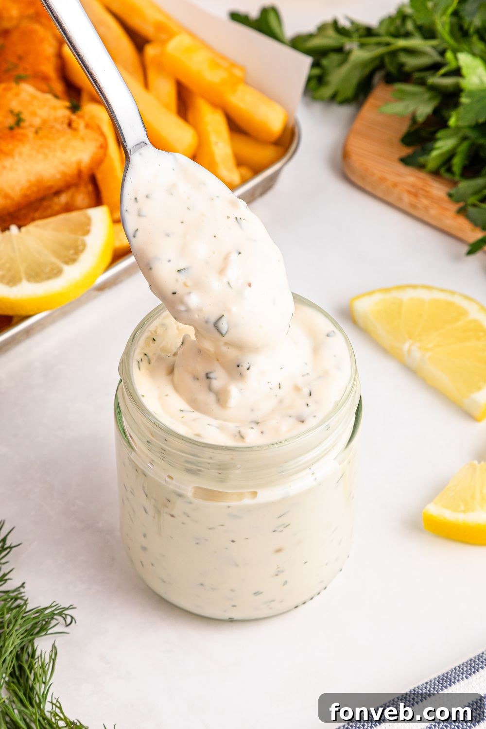 Effortless Homemade Tartar Sauce Beats Store Bought 8 Easy Homemade Tartar Sauce in a clear glass jar, with a spoon poised to lift out a spoonful, displaying its enticing texture.