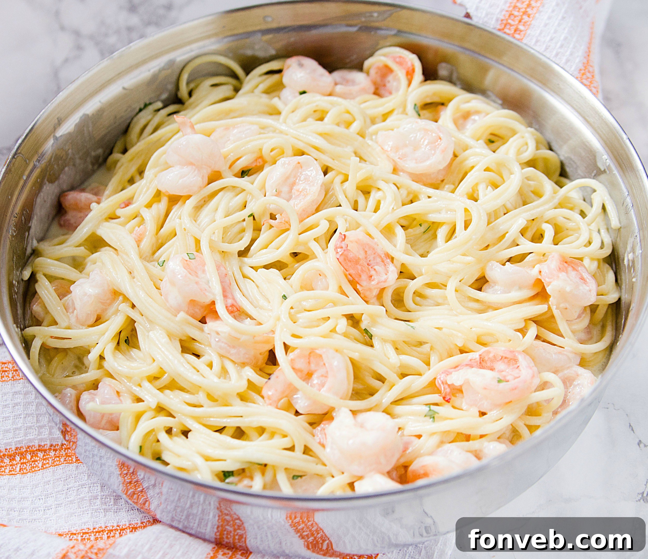 Cooked shrimp and pasta being tossed together in a large skillet, coated in the creamy sauce.