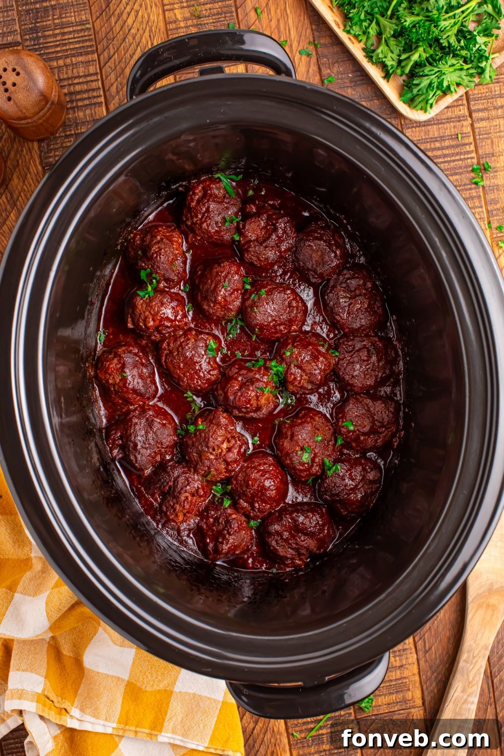 CrockPot sitting on table full of homemade cooked meatballs, with a twoel and garnish to the side of CrockPot