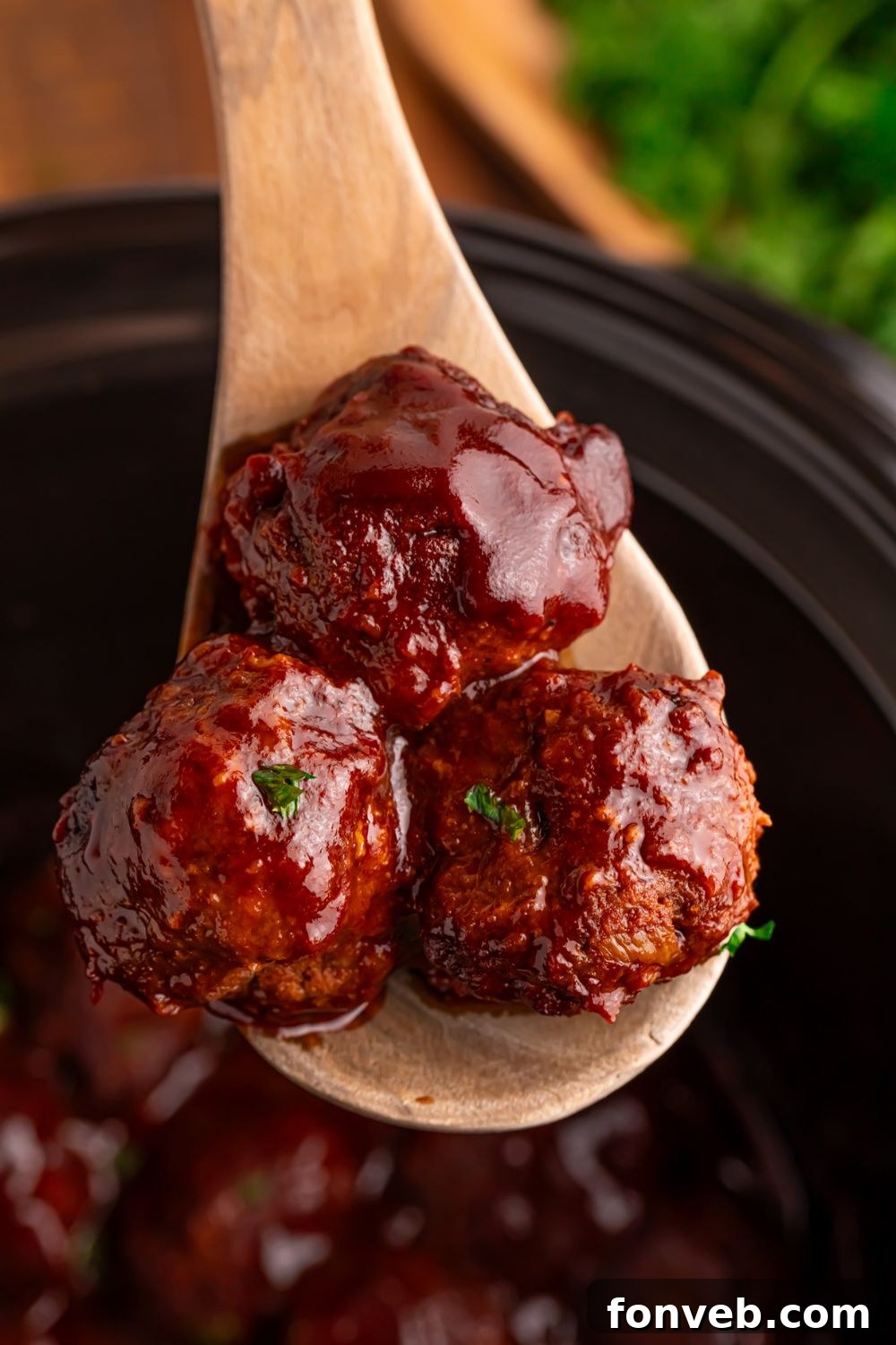 Crockpot Homemade BBQ Meatballs being lifted up out of CrockPot on a wooden spoon 