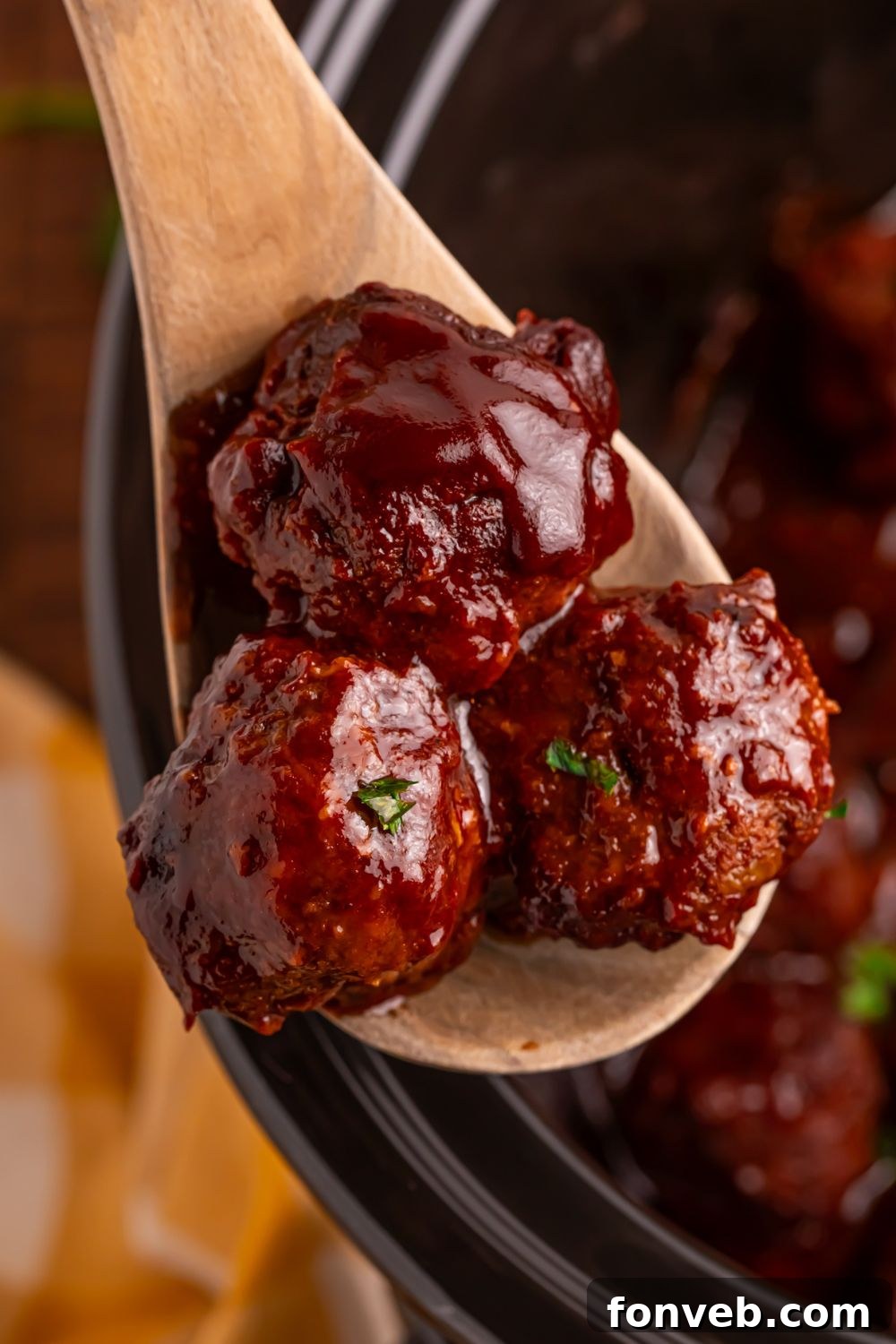 Crockpot Homemade BBQ Meatballs on a wooden spoon lifting up out of crockpot 