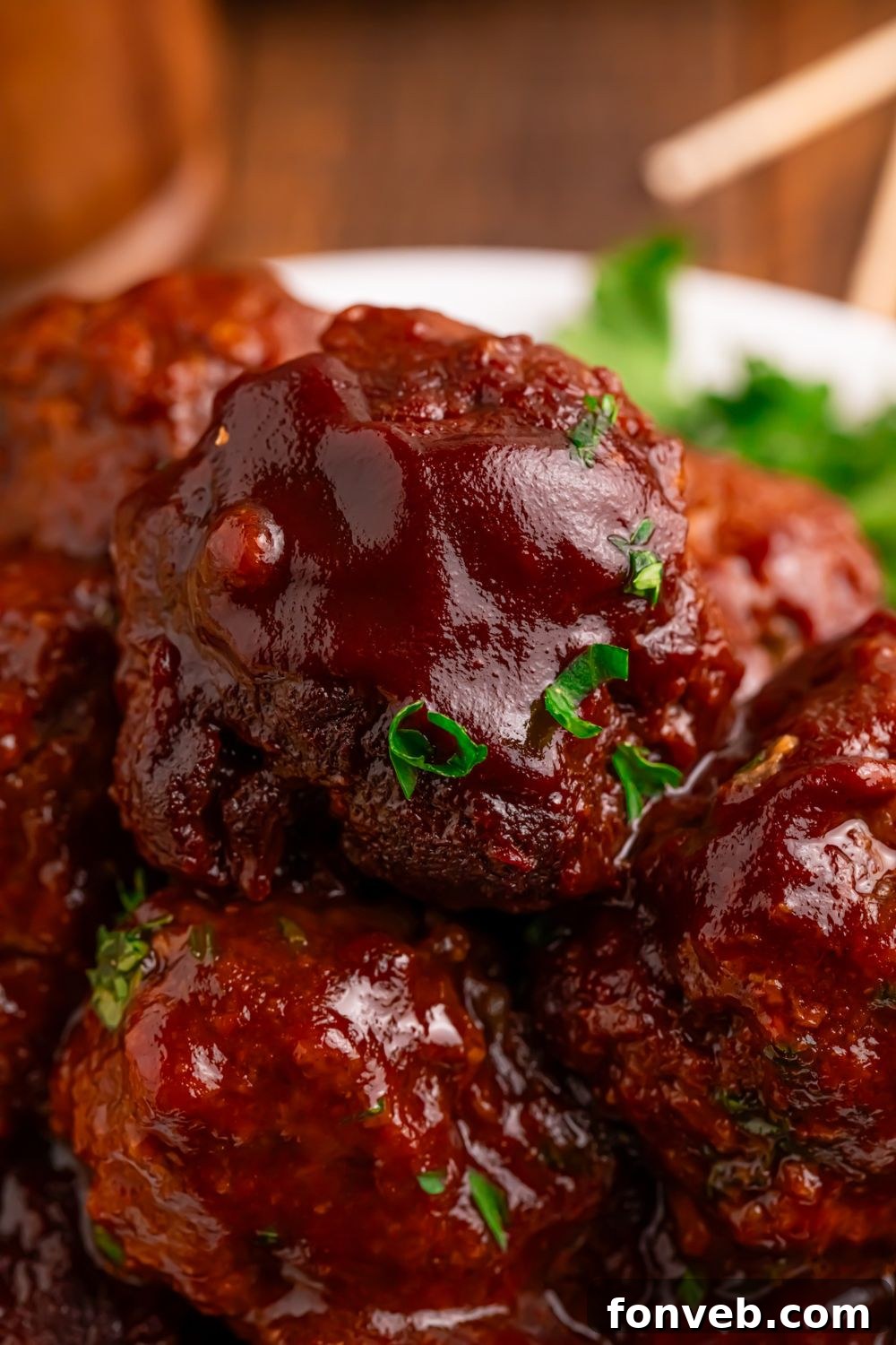 Crockpot Homemade BBQ Meatballs stacked on a plate with some garnish sprinkled on top 