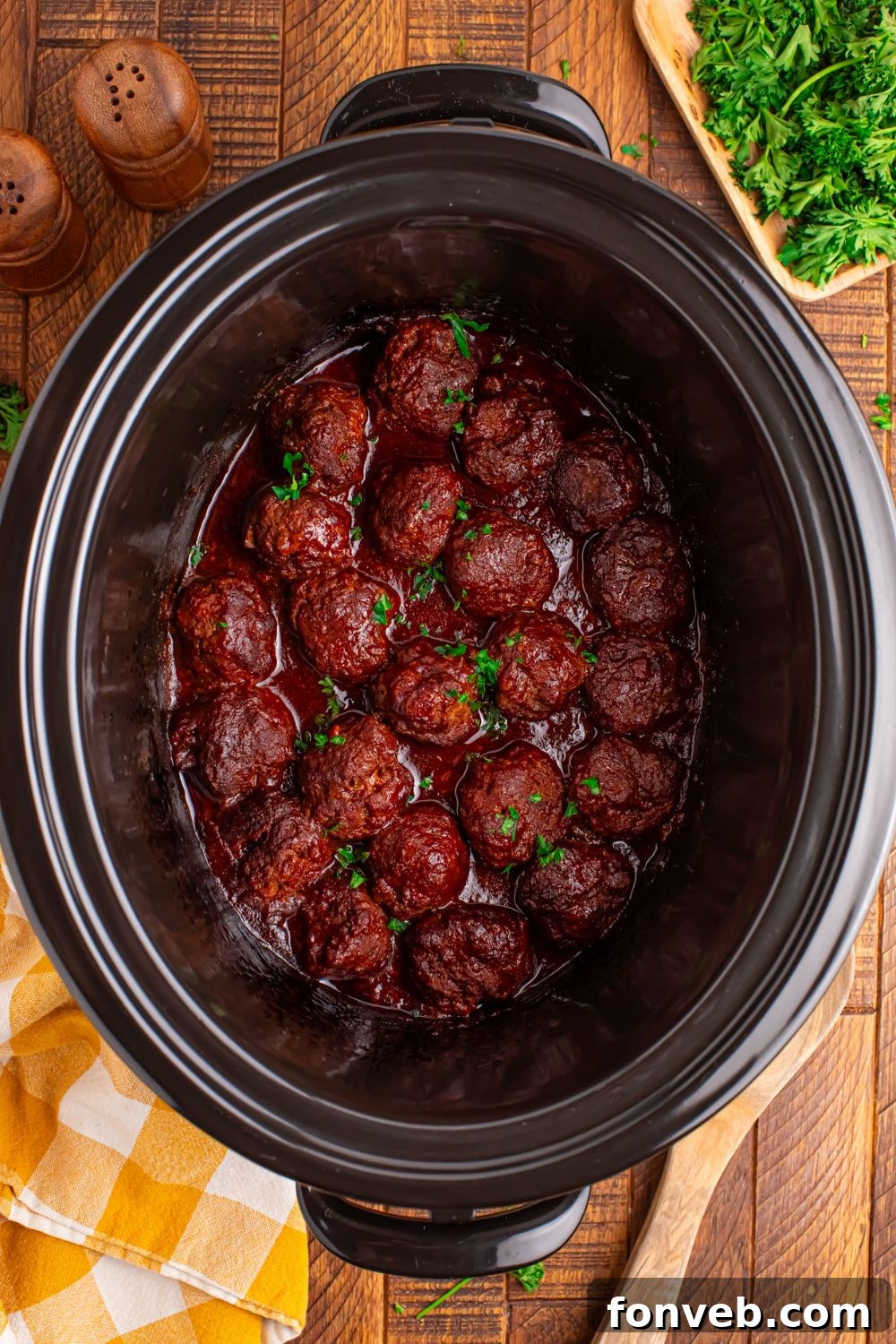 Crockpot Homemade BBQ Meatballs sitting on table with parsley, wooden spoon, and towel to side