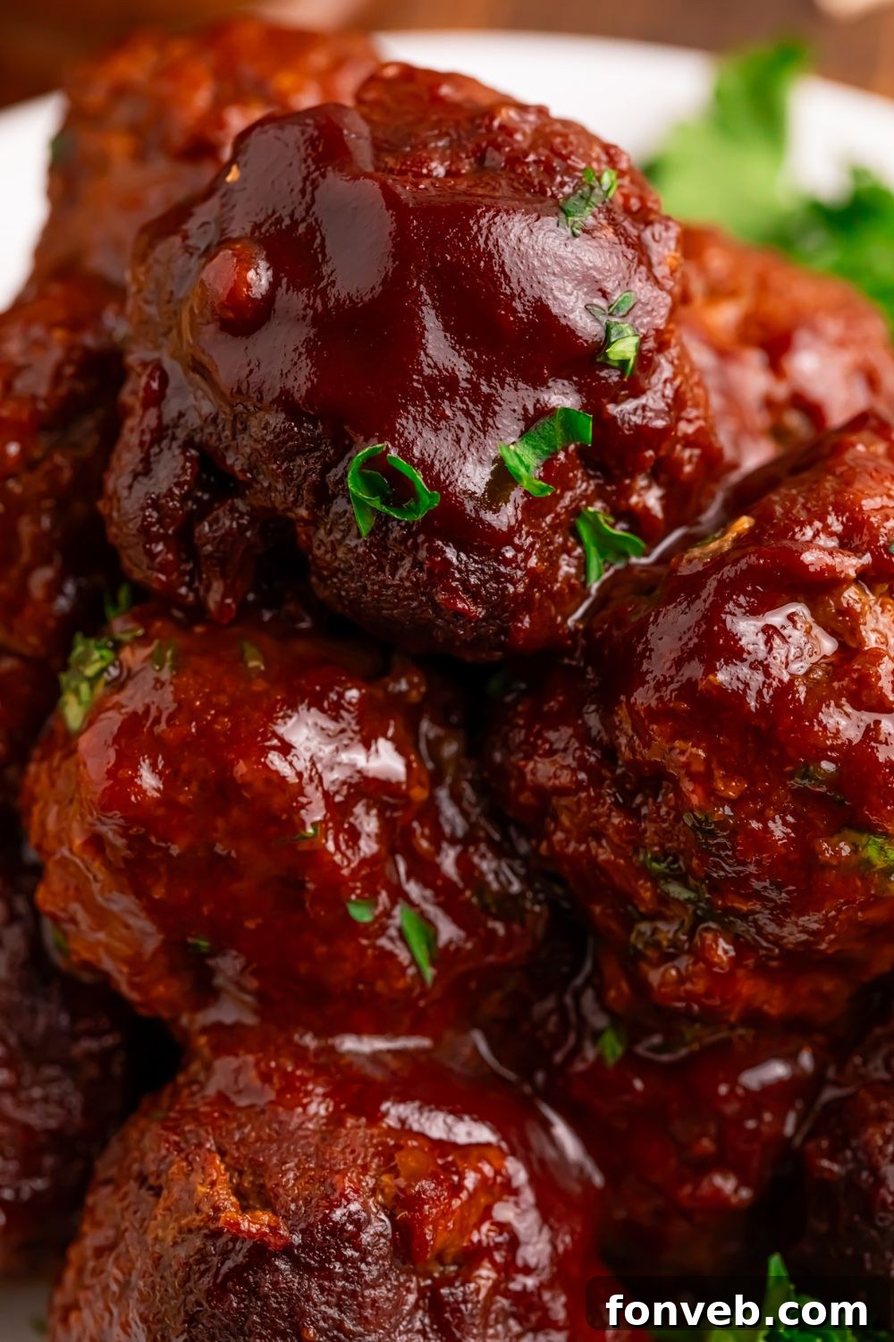 Crockpot Homemade BBQ Meatballs stacked on a plate with some fresh herbs on top 