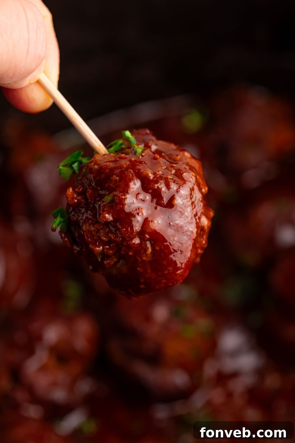 toothpick with a homemade bbq meatball on it above Crockpot
