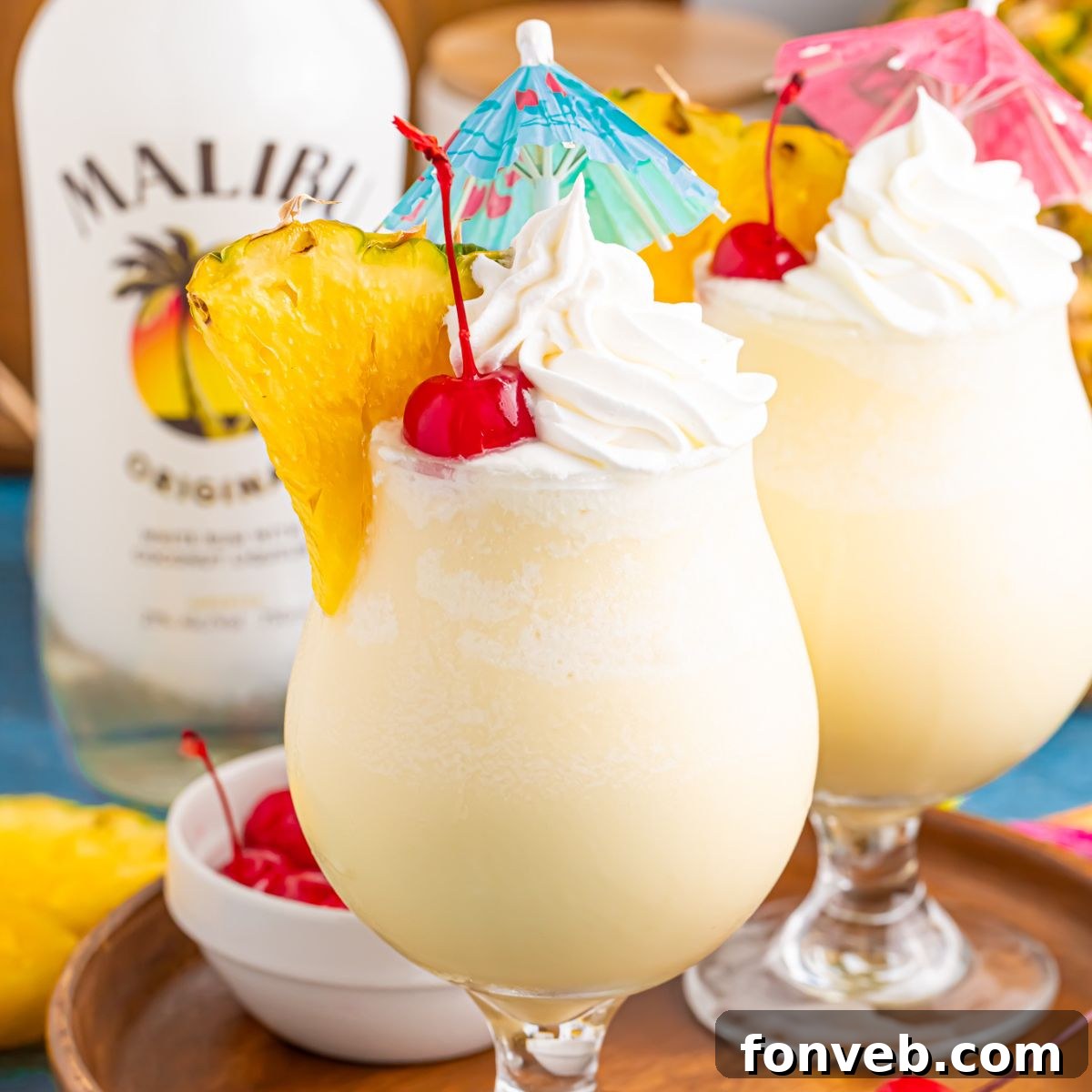 Creamy Frozen Malibu Piña Colada Delight 2 Frozen Malibu Piña Coladas in glasses with little umbrellas, pineapple slices and cherries