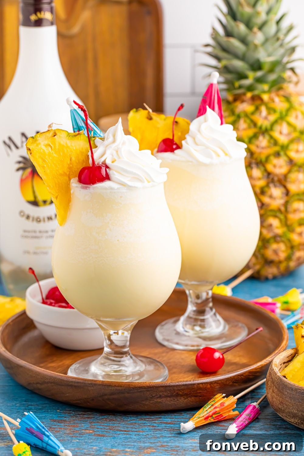 Creamy Frozen Malibu Piña Colada Delight 14 Frozen Malibu Piña Coladas on a tray with cherries and drink umbrellas scattered on table