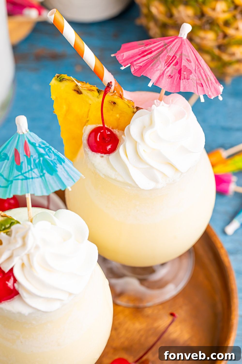 Creamy Frozen Malibu Piña Colada Delight 3 Frozen Malibu Piña Colada drinks on table with cherry, pineapple and umbrella in each glass on table
