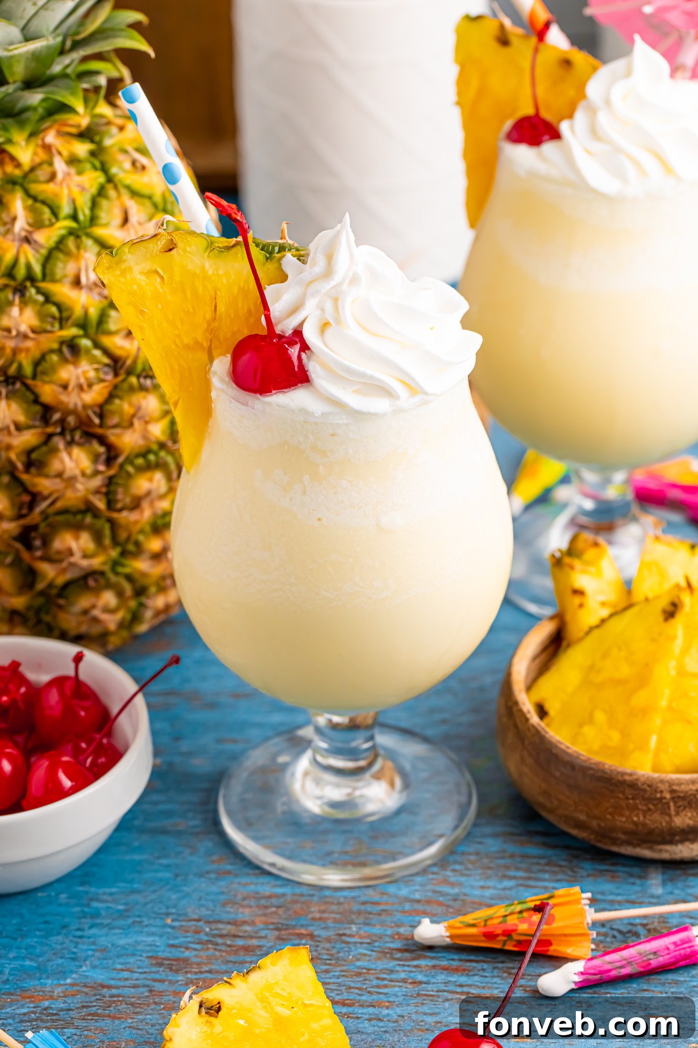 Creamy Frozen Malibu Piña Colada Delight 23 Frozen Malibu Piña Colada in a cocktail glass with a whole pineapple to side, bowl of cherries and pineapples
