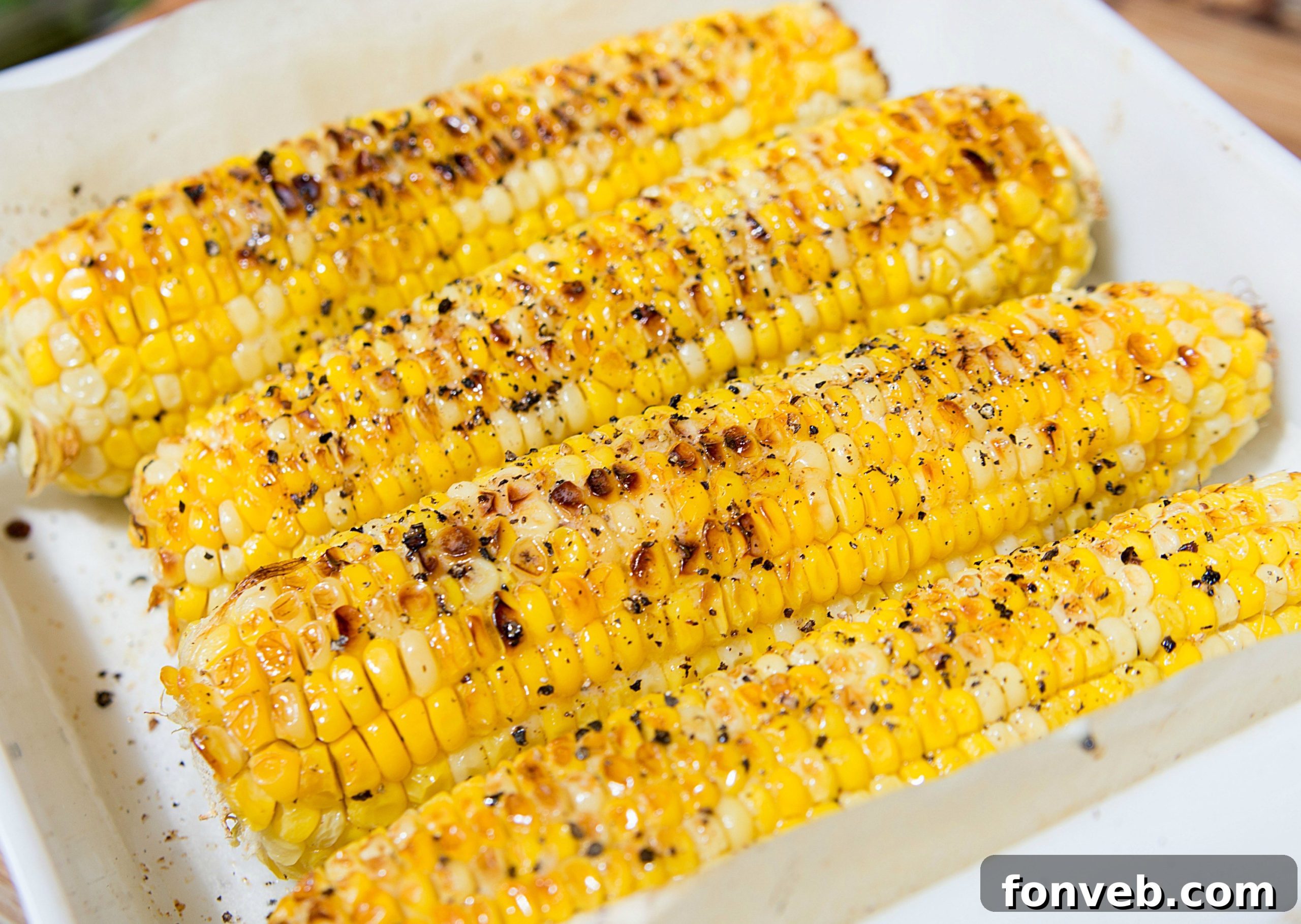 Close-up of freshly oven roasted corn on the cob, glistening with butter and spices on a wooden cutting board.