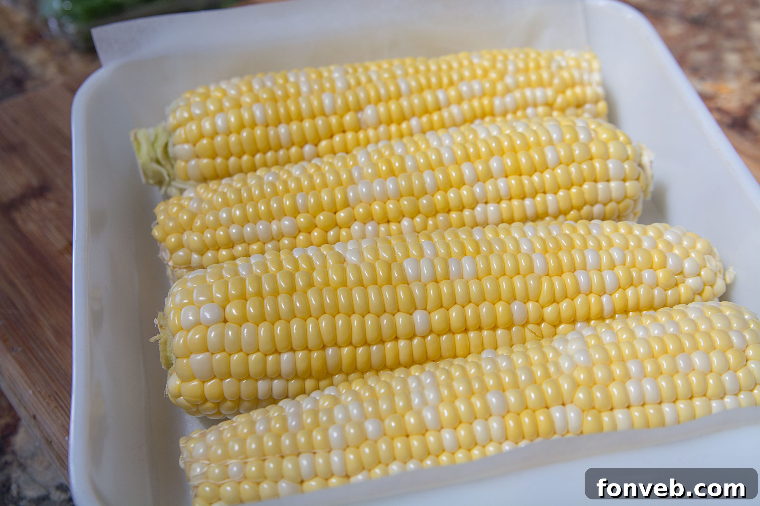 Several ears of corn on the cob, some with husks pulled back, displayed on a rustic surface, evoking summer freshness.