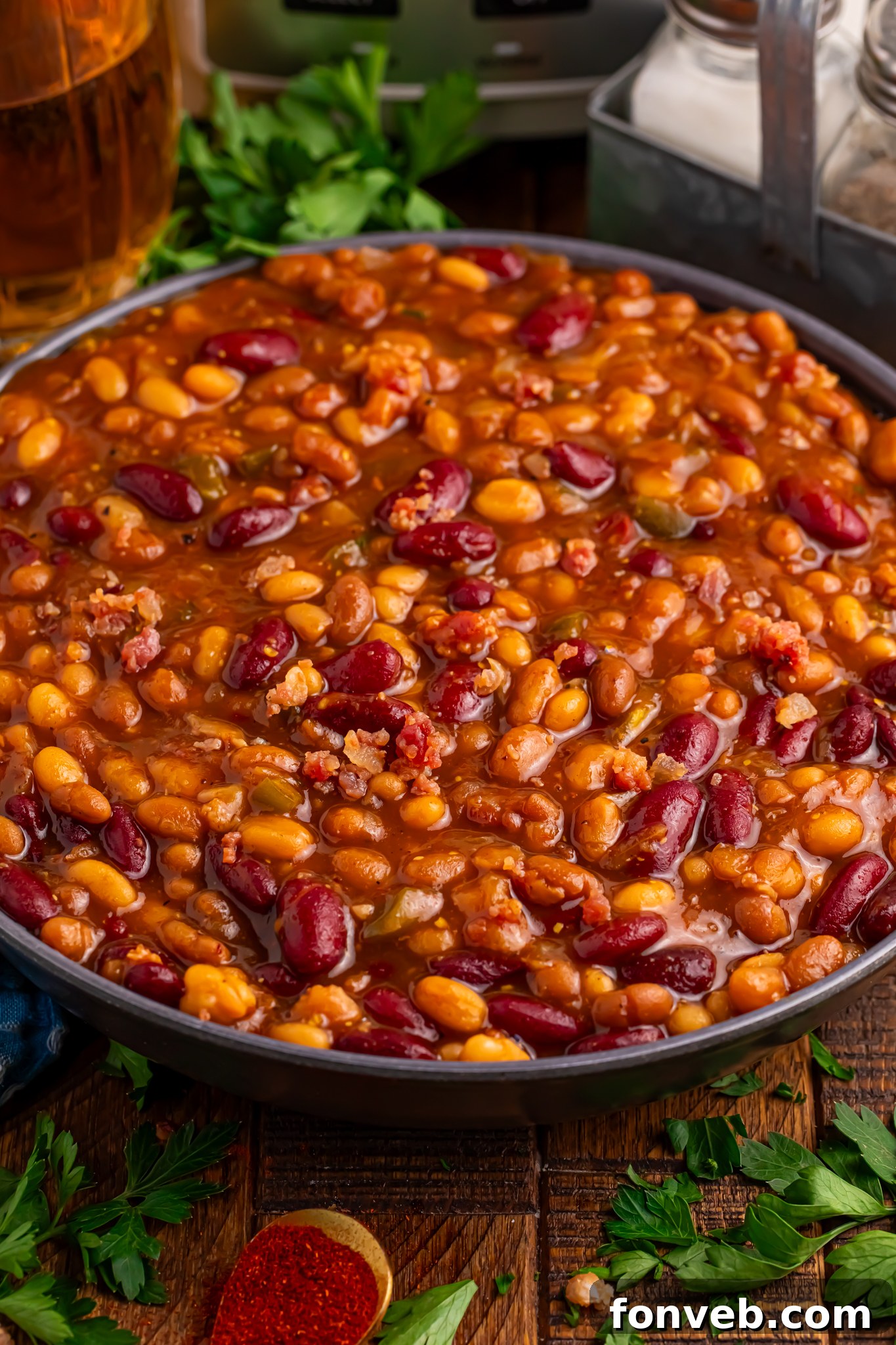 Crockpot Bourbon Brown Sugar Baked Beans in a bowl sitting on table with some fresh herbs to side of bowl