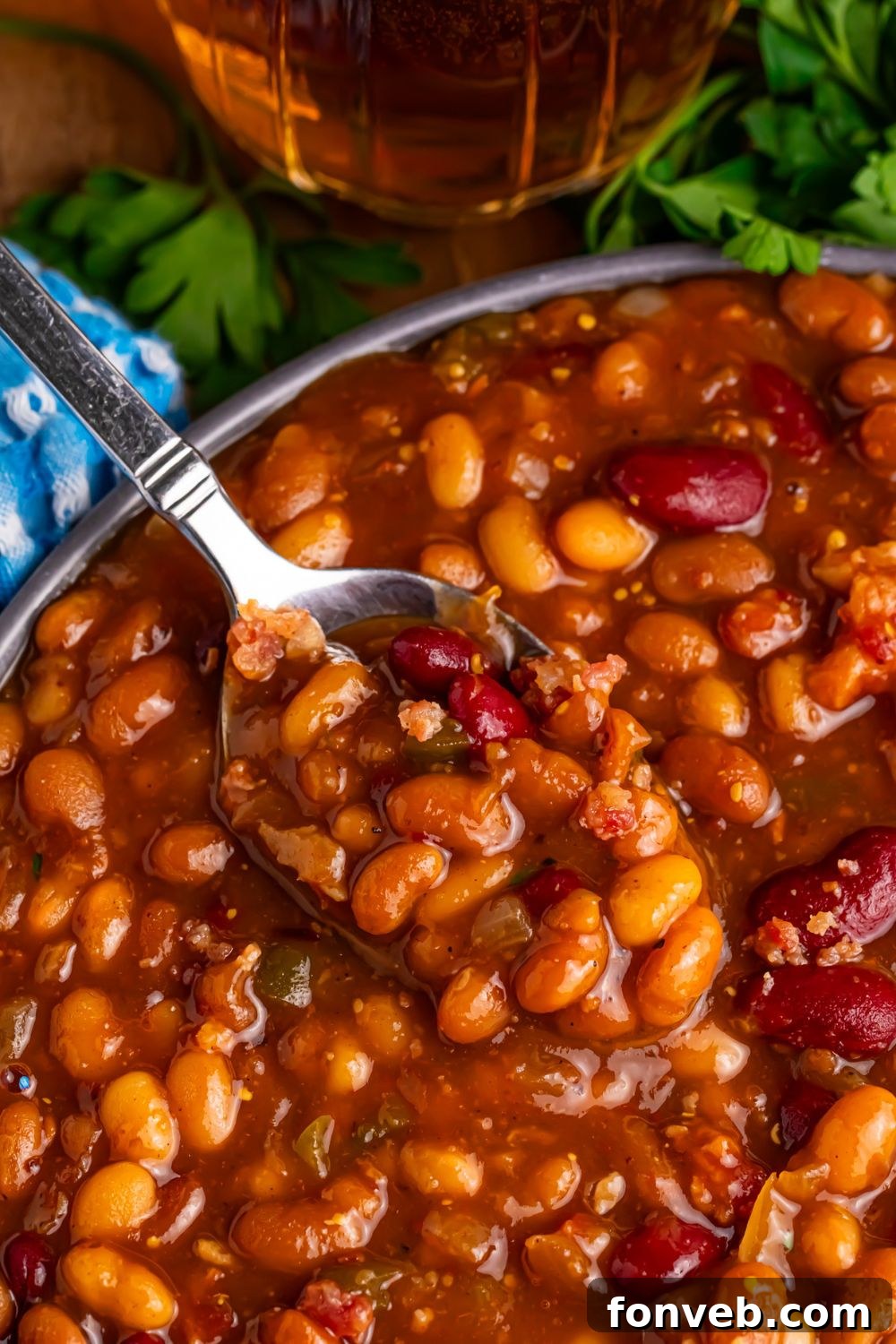 Crockpot bourbon baked beans in a bowl with a spoon scooping some out of bowl 