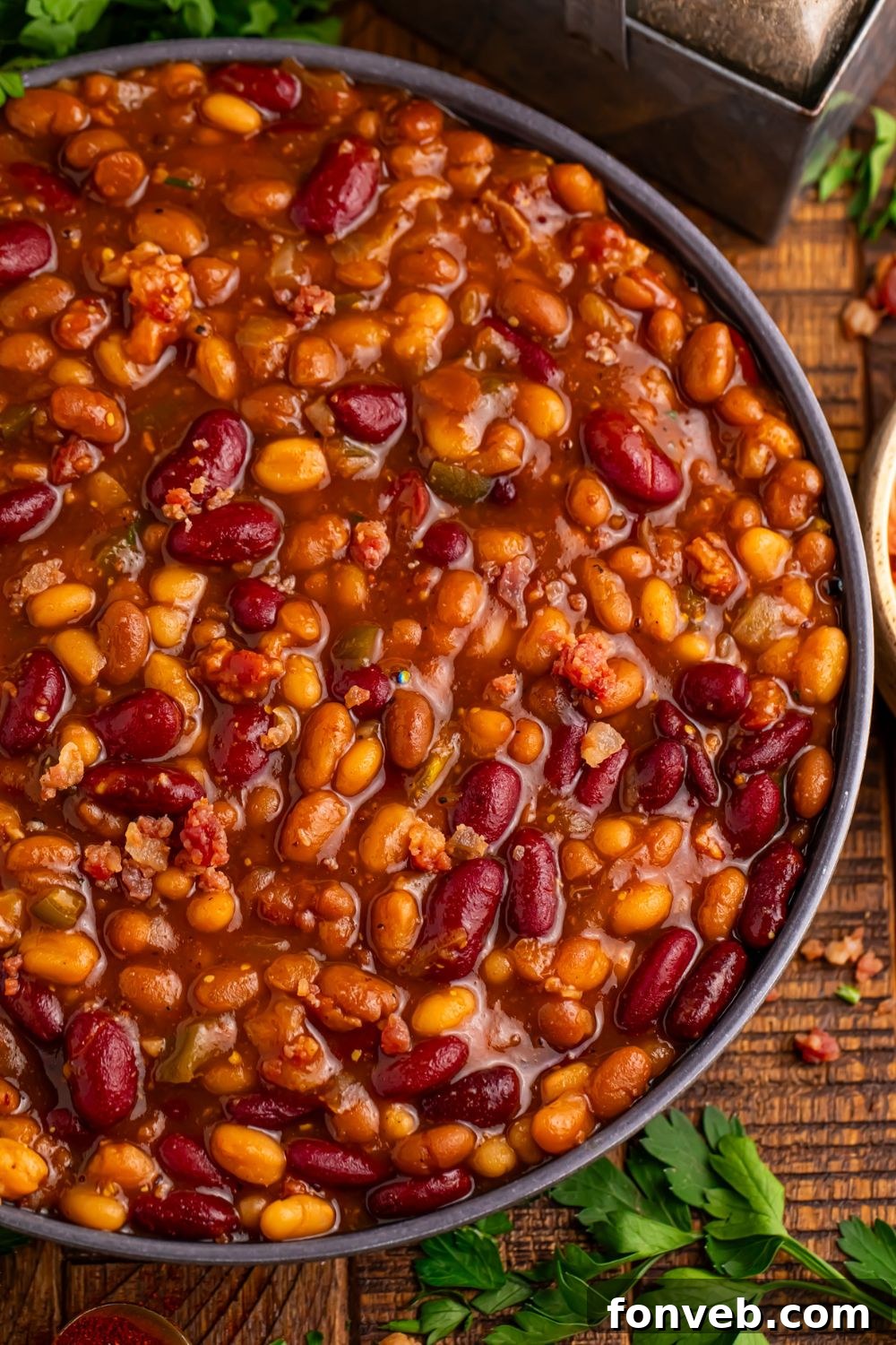 Crockpot bourbon baked beans in a bowl with some herbs around the bowl and salt and pepper 