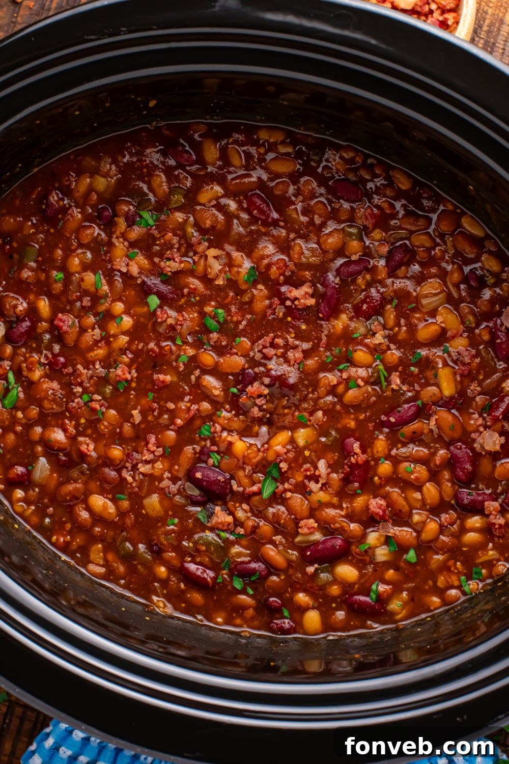 Crockpot with bourbon baked beans in it on table with a blue towel to side 